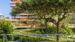 Un immeuble à plusieurs étages doté de balcons, entouré d’une végétation luxuriante et d’une clôture en métal.