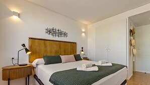 Une chambre d’hôtel avec un lit, deux lampes de chevet, une tête de lit en bois, une œuvre d’art murale et une porte sur laquelle sont accrochés des chapeaux.