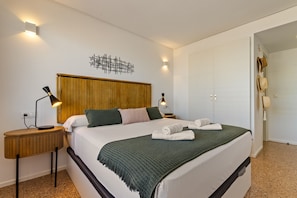 Ein Hotelzimmer mit Bett, zwei Nachttischlampen, einem Holz-Kopfteil, einem Wandbild und einer Tür mit hängenden Hüten.