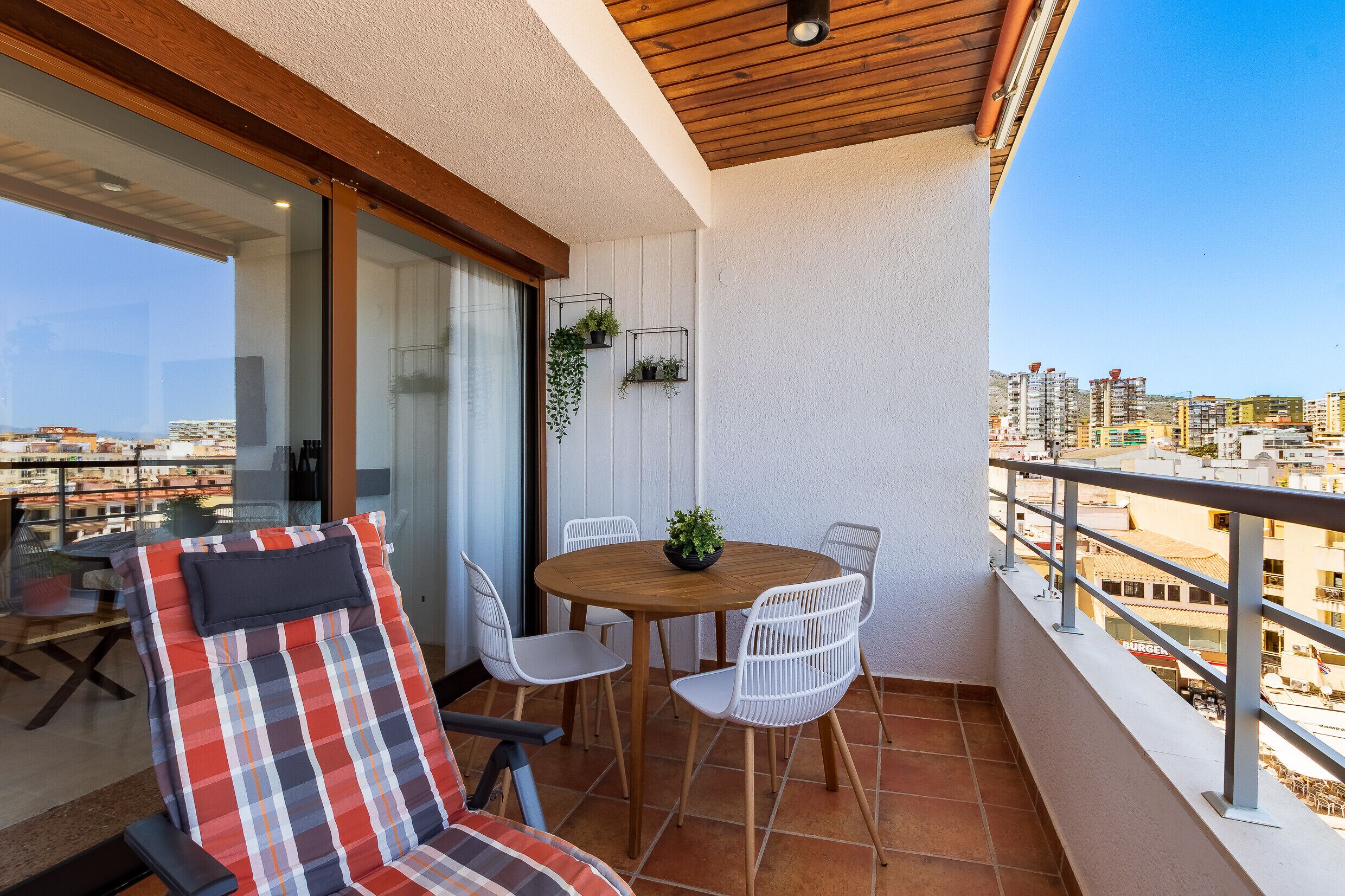 A balcony with a wooden table and chairs, a sofa, and a view of the cityscape.