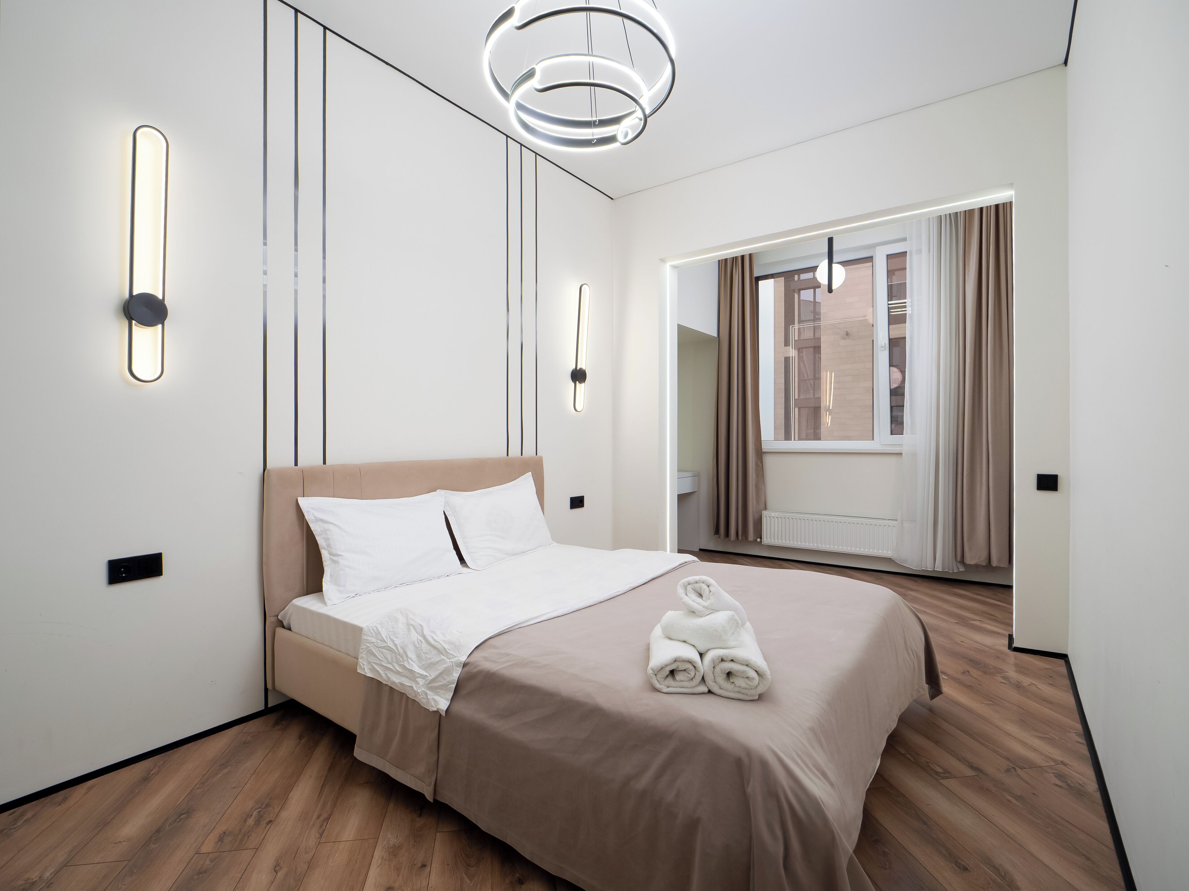 A modern hotel room with a bed, bedside lamps, a mirror, and a view of the outside.