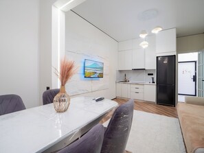 A modern kitchen with white cabinets, a black refrigerator, and a dining area with a marble table and purple chairs. - Cozy apartments in the business district (Almaty)