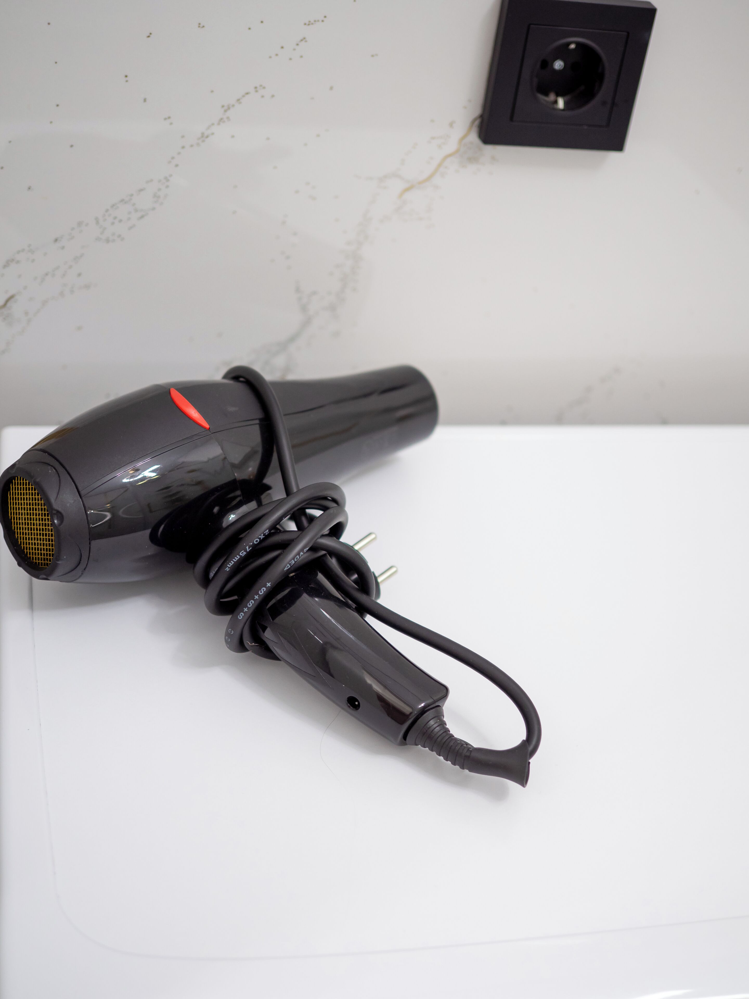 Un sèche-cheveux avec un cordon et une prise, posé sur une surface blanche.