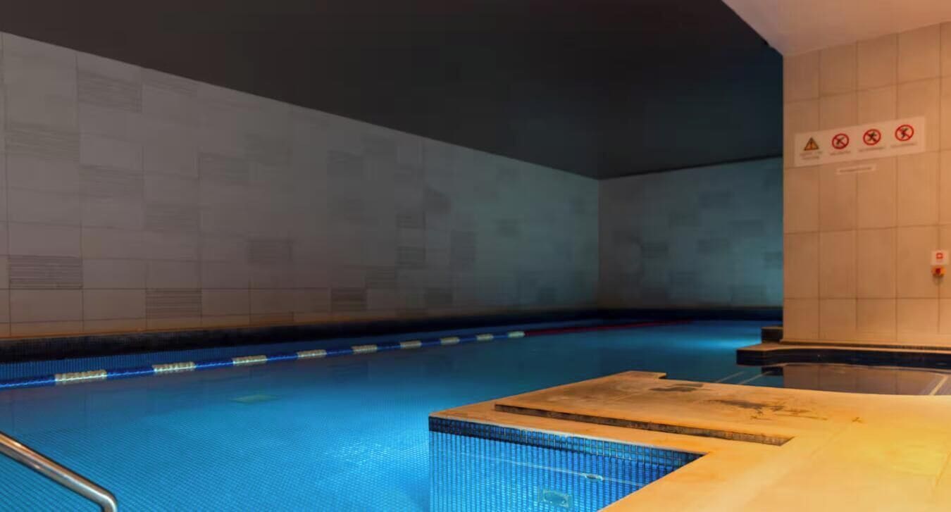 Ein Schwimmbecken mit gefliesten Wänden und einer Holzterrasse.