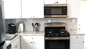 A kitchen with white cabinets, a microwave, a stove, and a coffee maker. - Cozy 2BR Apt 2 mi from Airport /PHL/ Free Parking (Prospect Park)
