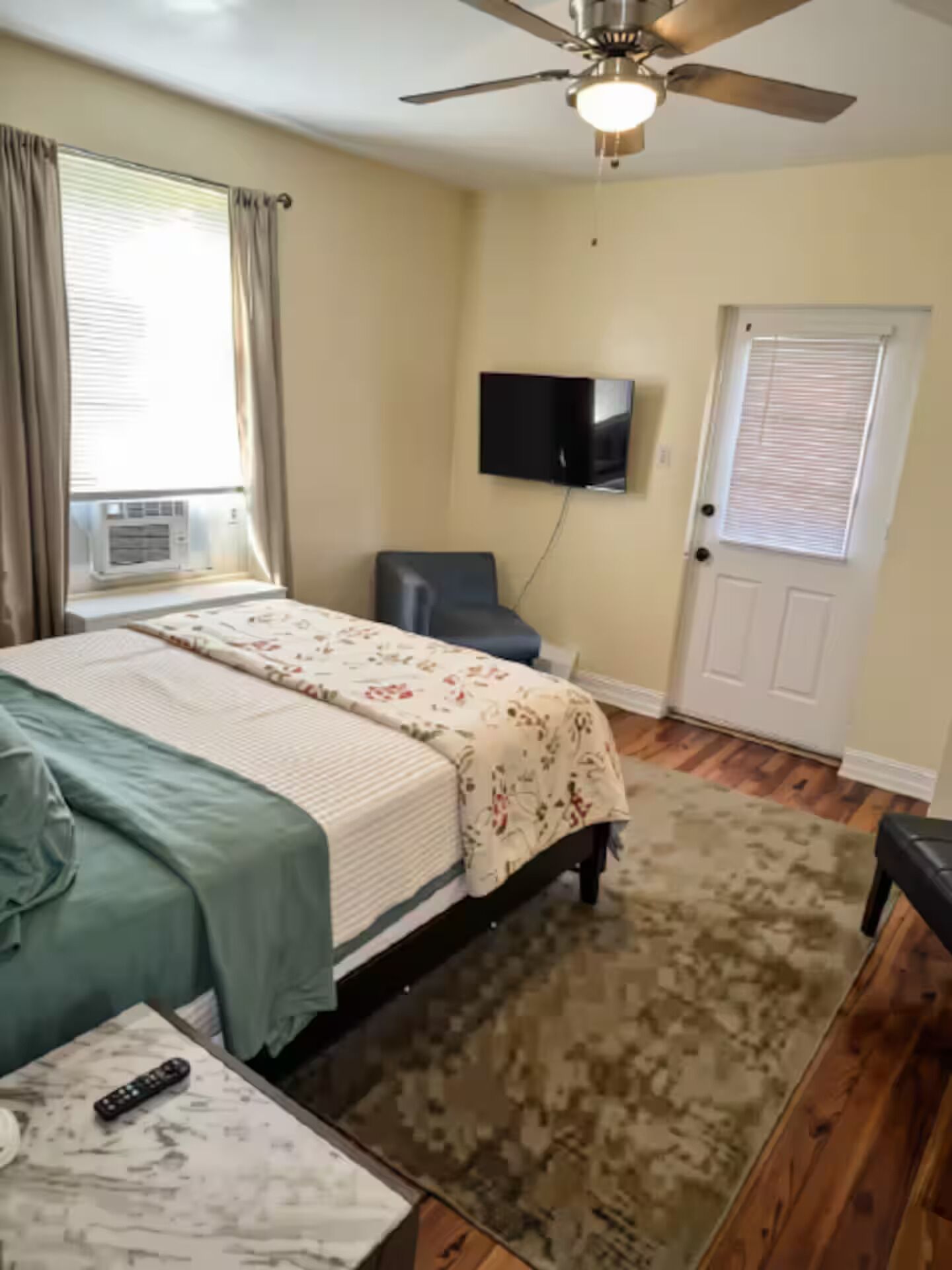 A bedroom with a bed, a chair, a television, and a ceiling fan.
