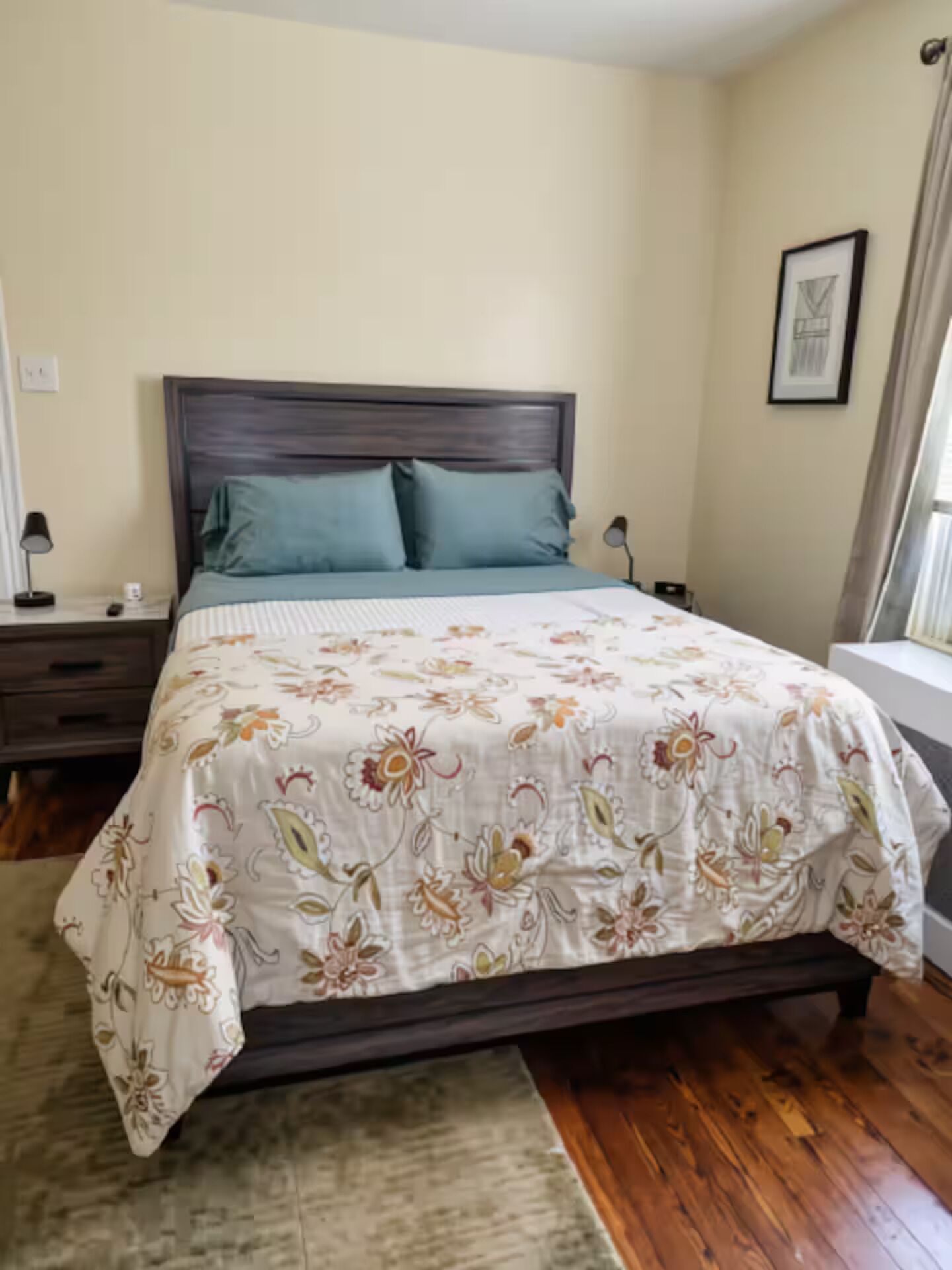 A bedroom with a bed, nightstands, a window with curtains, and a framed picture on the wall.