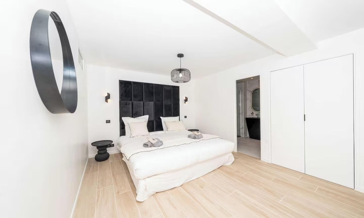 Un dormitorio moderno con una cama grande, un reloj de pared redondo, una lámpara colgante y un vestidor.