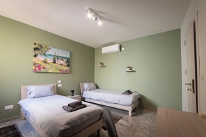 A bedroom with two beds, a painting, an air conditioning unit, and a door. - Peaceful Gozo Penthouse with Pool (Il-Qala)