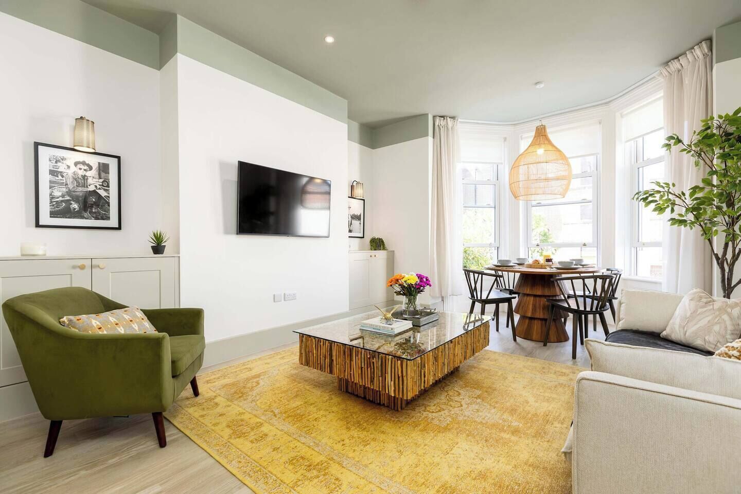 A modern living room with a green armchair, a glass coffee table, and a dining area with a round table and chairs.