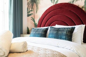 Ein Bett mit roter, gepolsterter Kopfteil, wei ßer Bettwäsche und zwei gemusterten Kissen.