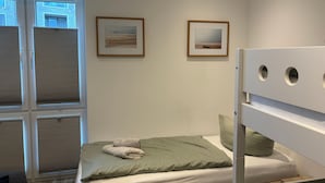Ein Schlafzimmer mit einem Bett, zwei gerahmten Bildern, einem Fenster mit Jalousien und einem Etagenbett.