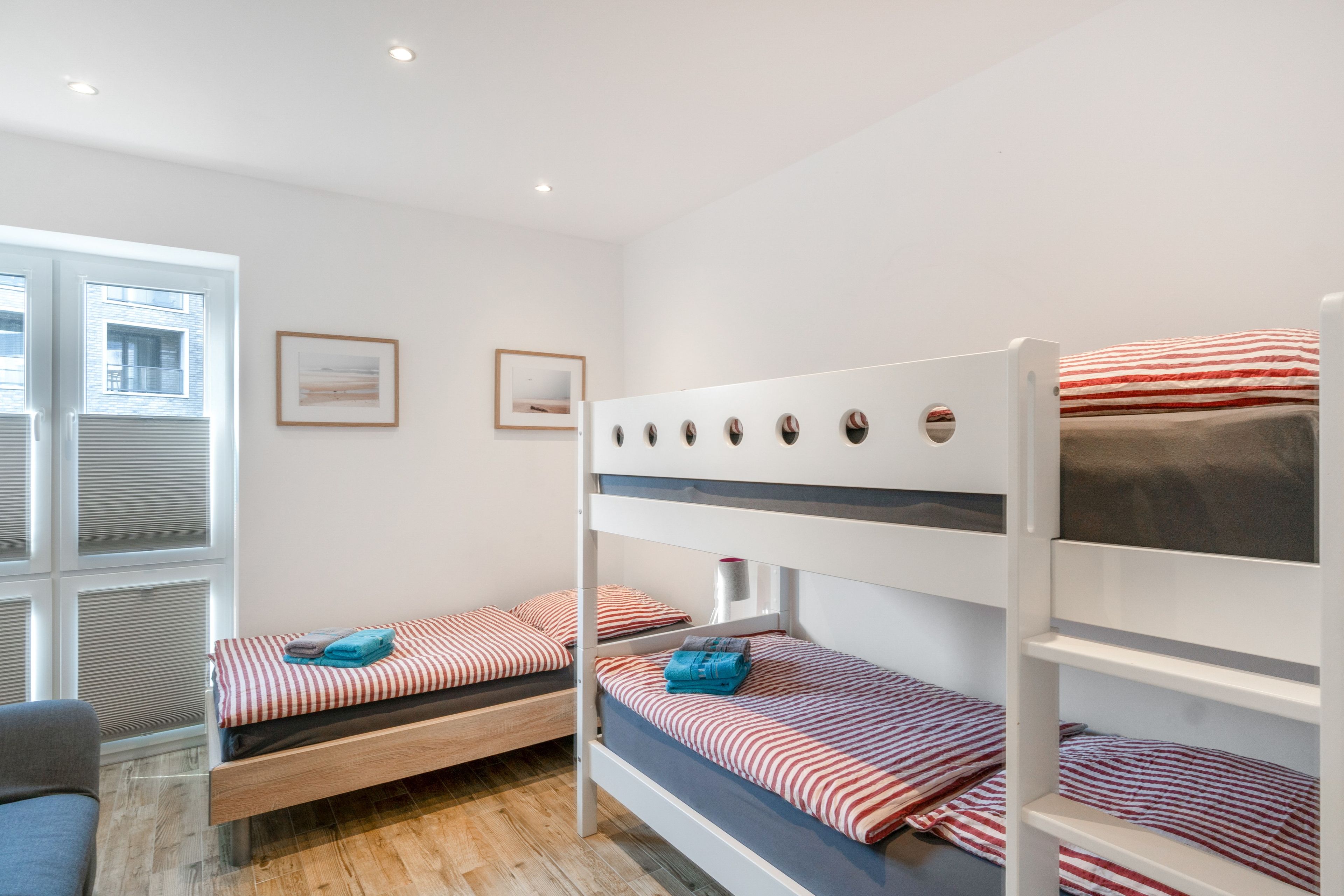 A room with bunk beds, a window with blinds, and a framed picture on the wall.