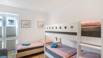 A room with bunk beds, a window with blinds, and a framed picture on the wall.