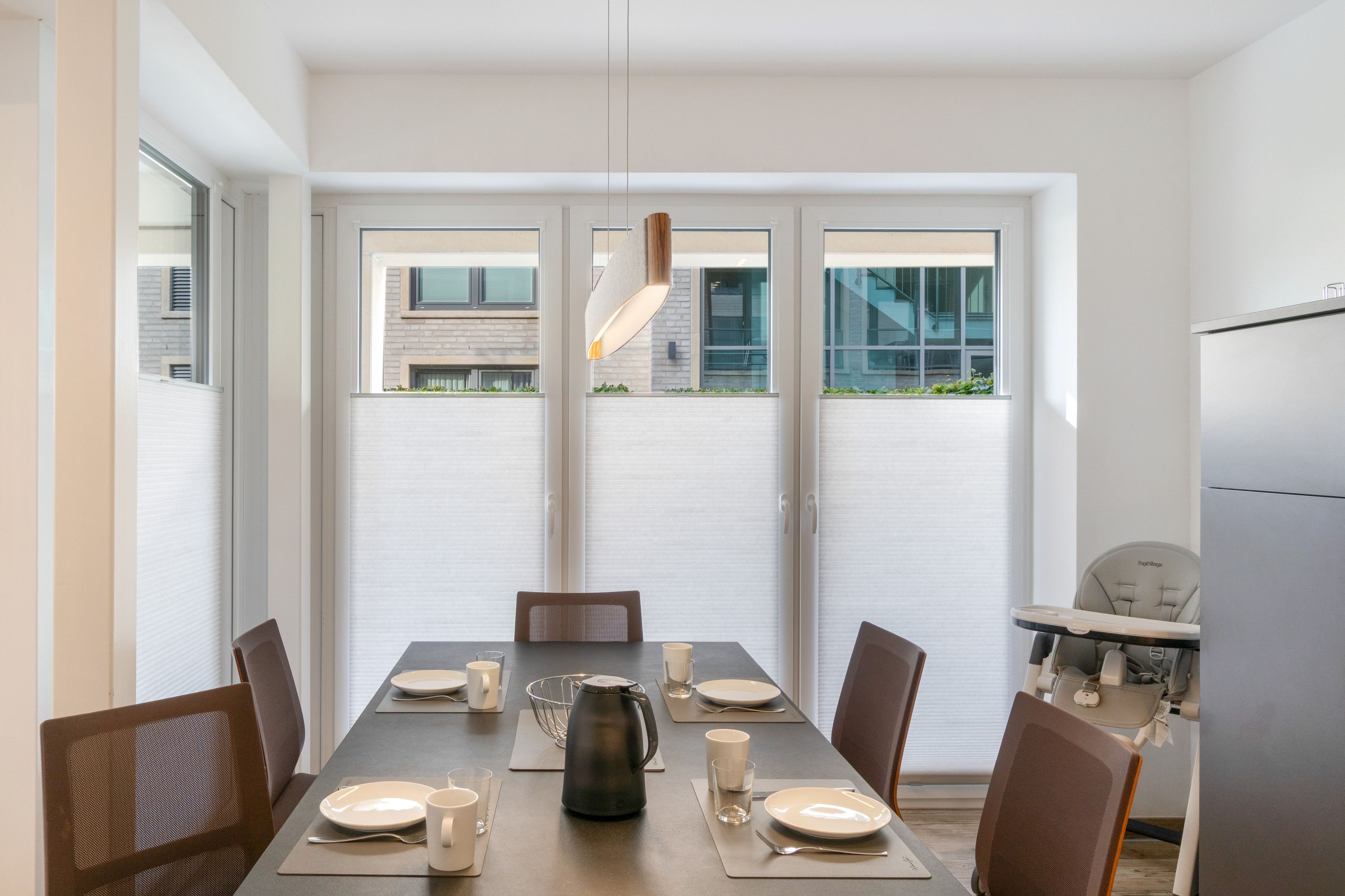 A dining area with a table set for four, chairs, a kettle, and a refrigerator in the background.