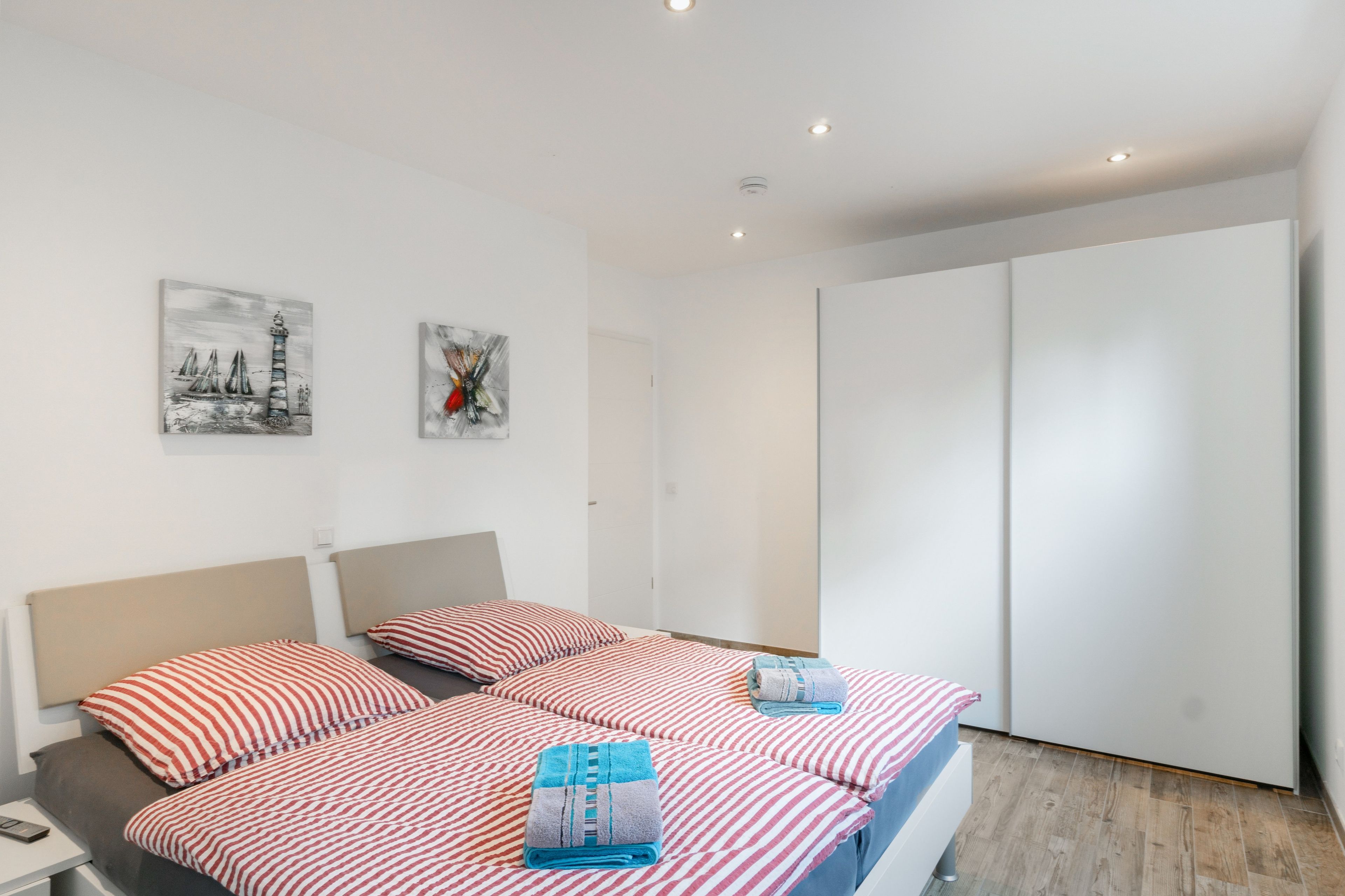 Ein Hotelzimmer mit einem Bett, zwei Kissen, einem Nachttisch, einer Lampe, einem Telefon und zwei Kunstwerken an der Wand.