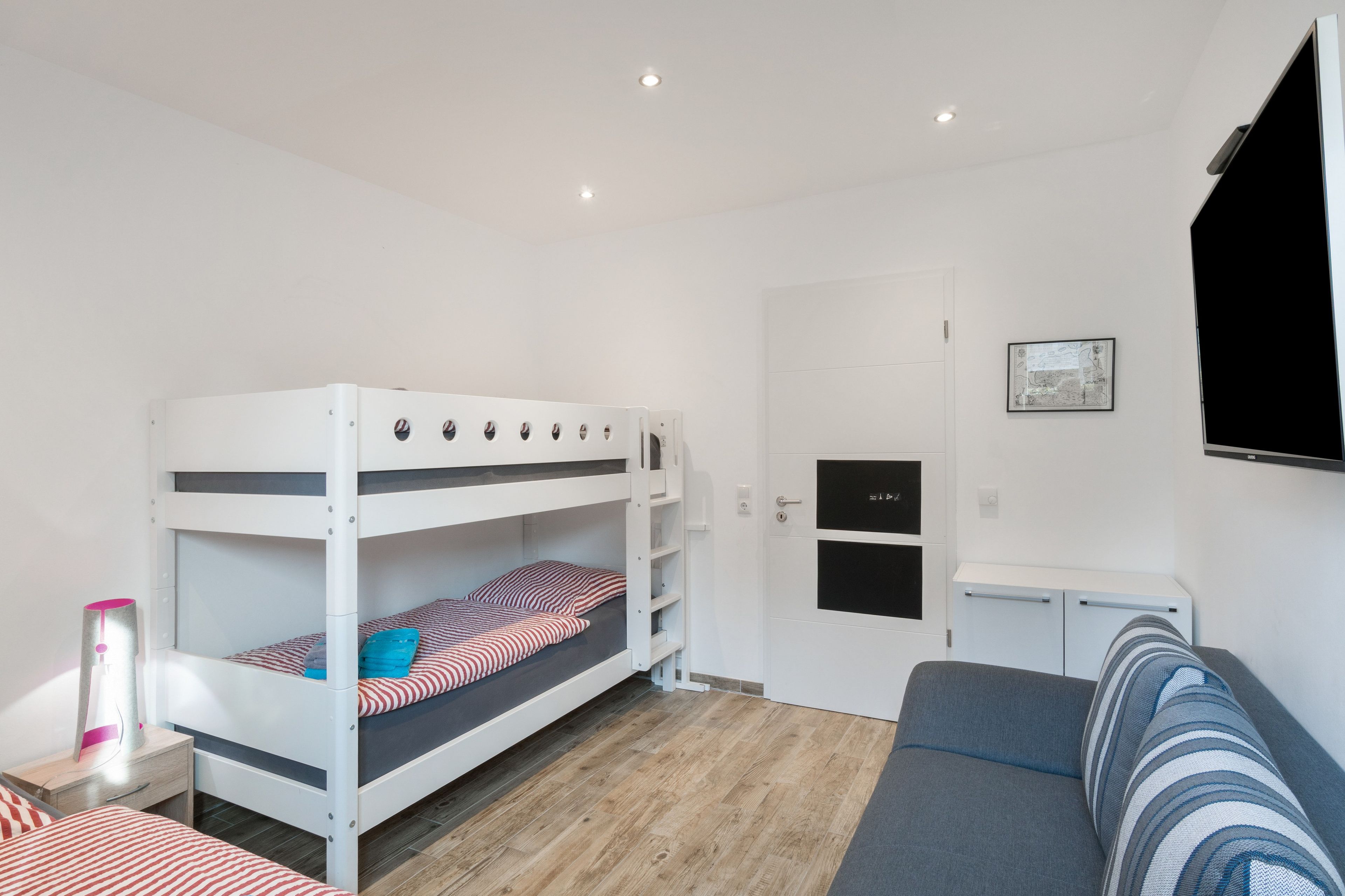 Una cama litera con escritorio y sofá en una habitación con paredes blancas y suelo de madera.