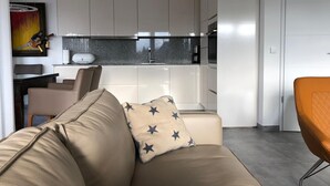 A modern living room with a sofa and a chair, a kitchen with white cabinets and a granite countertop, and a painting on the wall. - Apartment "Strandzeit" in Nordsee Park Dangast with Balcony and Private Sauna (Varel)