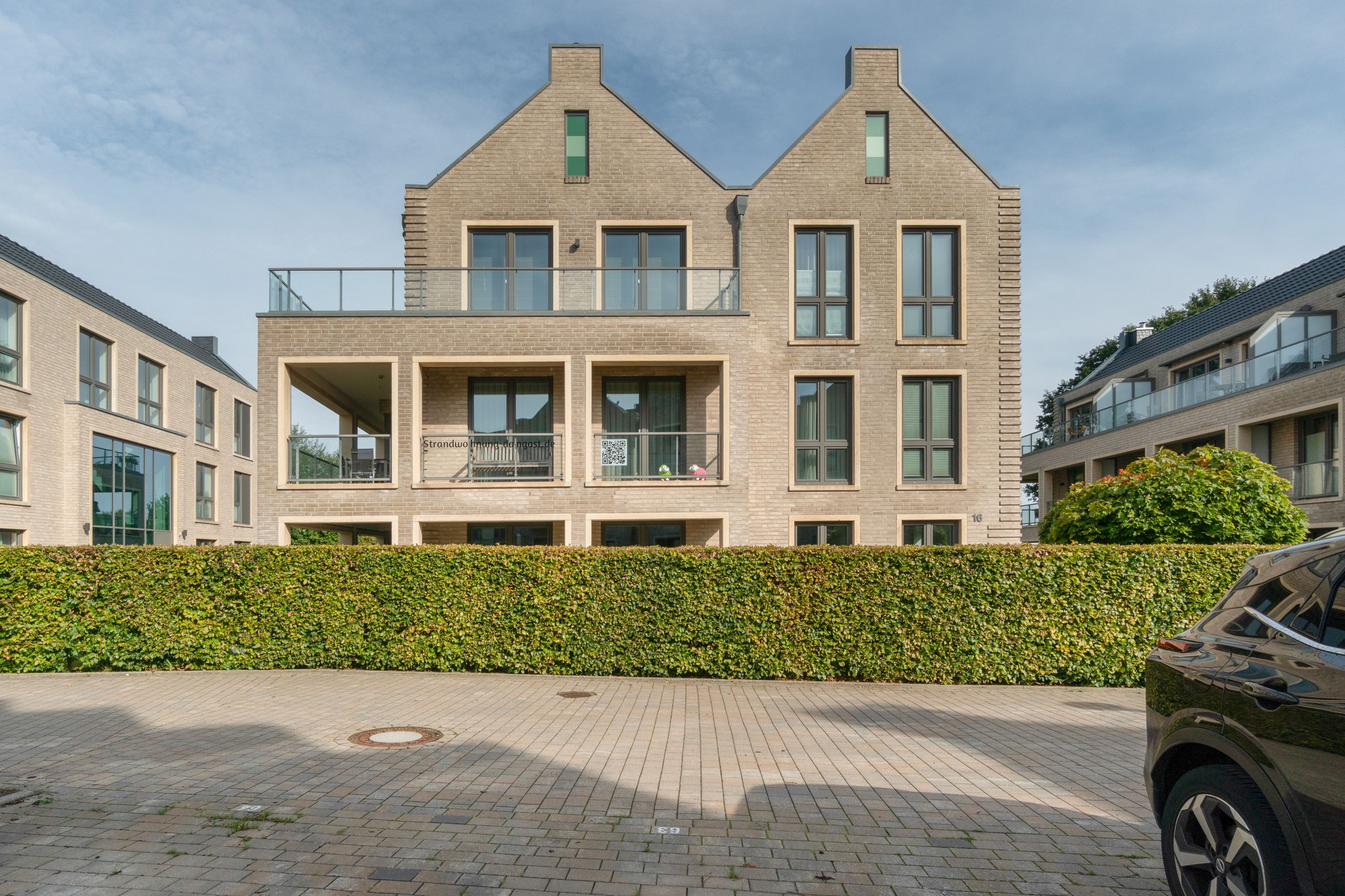 A modern two-story residential building with a brick facade, large windows, and a balcony.