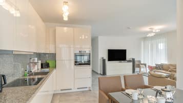 A modern kitchen with built-in appliances, a dining area with a table set for two, and a living room with a flat-screen TV and seating.