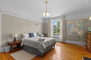 A neatly arranged bedroom with a bed, bedside tables, a lamp, a map on the wall, and a window with curtains. - Grand Heritage Home on Gower | 4BR (St. John's)