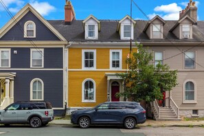 A row of townhouses with a garage, a tree, and a person on the sidewalk. - Grand Heritage Home on Gower | 4BR (St. John's)