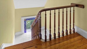 Eine Holztreppe mit weißer Decke und Blick auf ein blau gerahmtes Fenster.