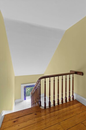 A wooden staircase with a white ceiling and a view of a blue-framed window. - Grand Heritage Home on Gower | 4BR (St. John's)
