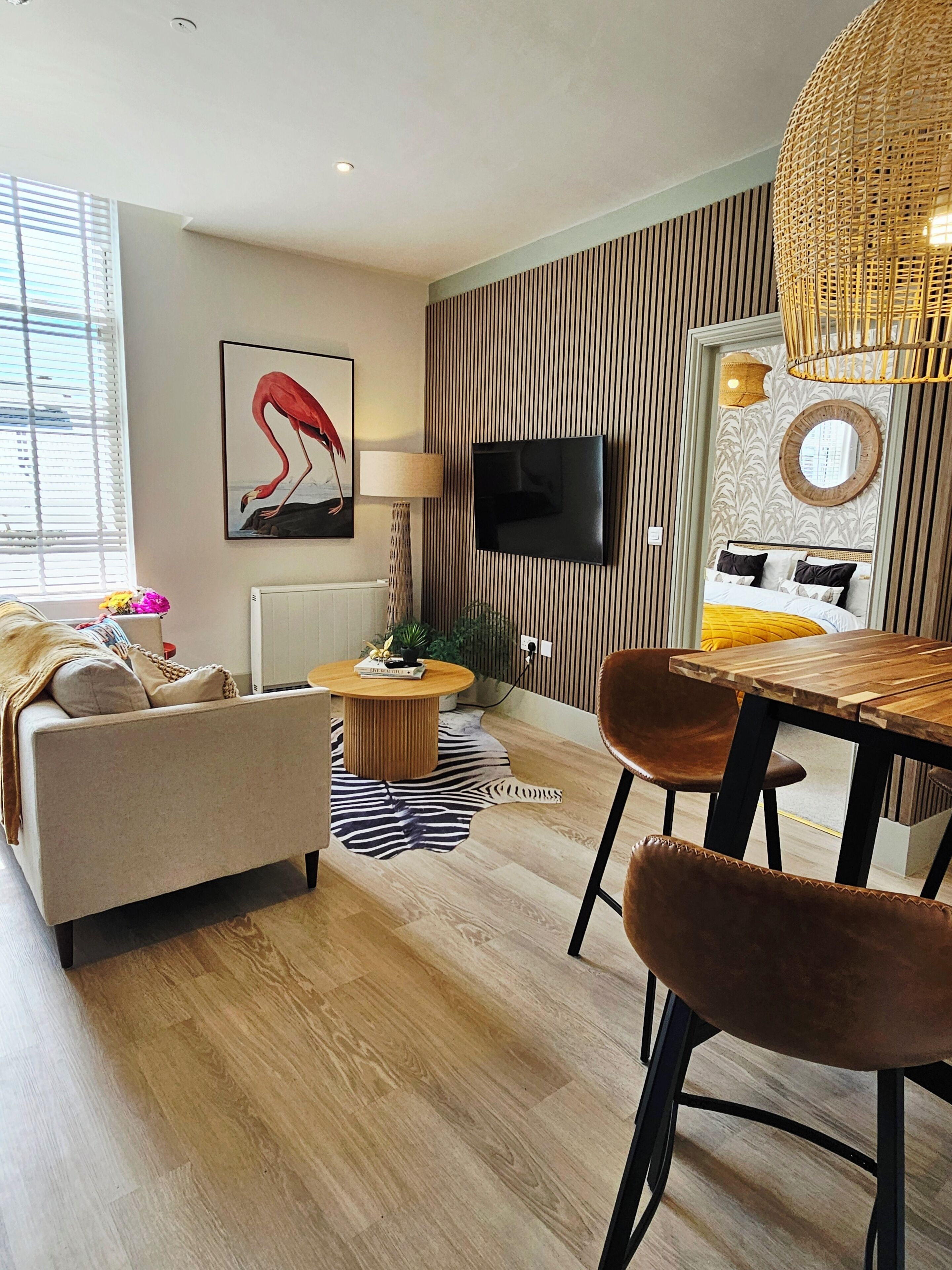 A modern living room with a sofa, a round coffee table, a dining table with chairs, a television mounted on the wall, and a patterned wallpaper.