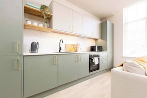 A modern kitchen with light green cabinets, a built-in oven, a microwave, and a coffee maker.