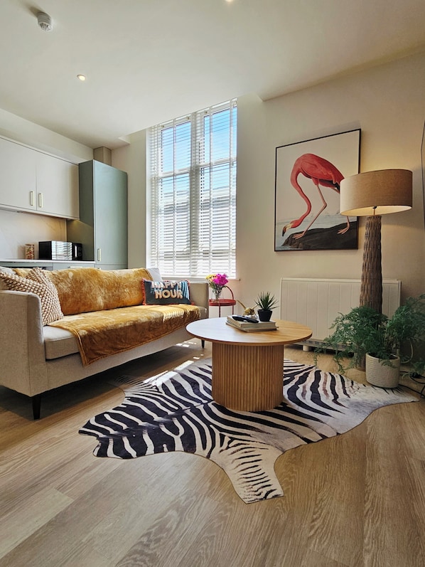A modern living room with a sofa, a round coffee table, a zebra-patterned rug, and a large window with blinds.
