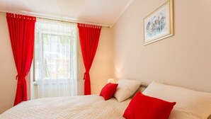 Ein Schlafzimmer mit einem Bett, roten Vorhängen, einem Gemälde und einem Fenster.