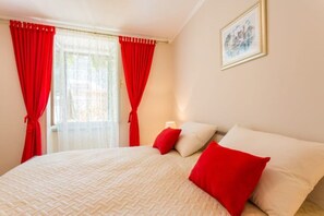 Ein Schlafzimmer mit einem Bett, roten Vorhängen, einem Gemälde und einem Fenster.