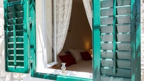 Ein Zimmer mit einem Bett, einem Fenster mit grünen Lamellen und einem weißen Vorhang.