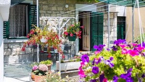 Ein Steinhäuschen mit Balkon, grünen Fensterläden und blühenden Blumenkörben.