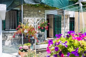Ein Steinhäuschen mit Balkon, grünen Fensterläden und blühenden Blumenkörben.