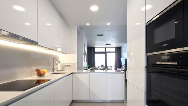 Una cocina moderna con muebles blancos, encimera negra y horno Bosch.