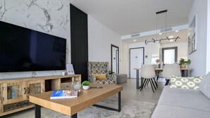 Una sala de estar moderna con una televisión de pantalla plana, una mesa de centro de madera, un sofá y un comedor con sillas.