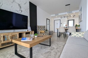 A modern living room with a flat-screen TV, a wooden coffee table, a sofa, and a dining area with chairs. - SUNSET SAILORS prestige apartment (Benidorm)