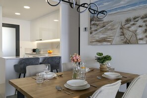 Un coin repas avec une table en bois dressée pour quatre personnes, entourée de chaises, et une cuisine en arrière-plan.