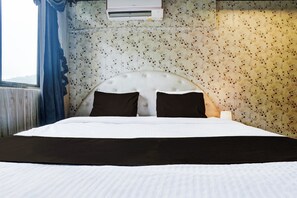 A hotel room with a bed, a window with curtains, a wall-mounted air conditioner, and floral wallpaper.