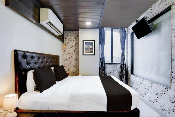 A bedroom with a large bed, a mounted air conditioner, a framed picture on the wall, and a window with curtains.