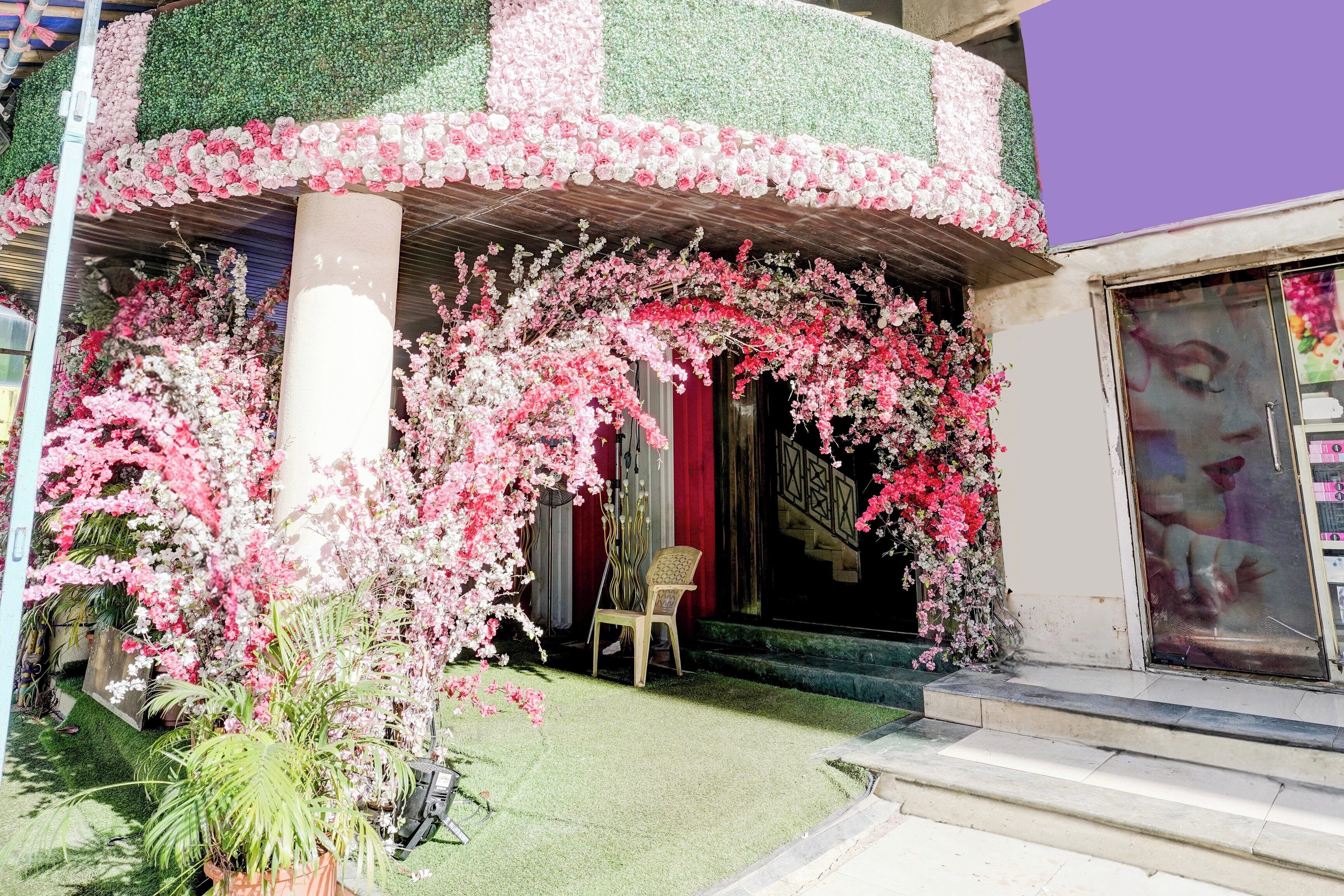 Fachada de edificio con diseño floral en tonos verde y rosa, una cortina roja y una silla afuera.