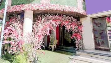 Fachada de edificio con diseño floral en tonos verde y rosa, una cortina roja y una silla afuera.