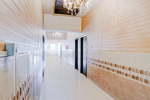 A long, narrow hallway with a high ceiling, a chandelier, and a view into a room at the end.