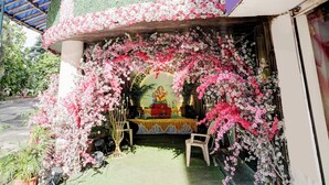 Un santuario al aire libre con una estatua, rodeado de flores rosas y blancas, bajo una estructura cubierta.