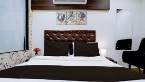 Habitación de hotel con una cama grande, cabecera, dos almohadas, mesita de noche, lámpara, silla y aire acondicionado instalado en la pared.