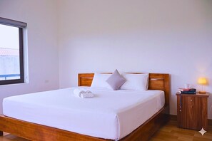 A neatly made bed with a wooden headboard and white bedding, a bedside table with a lamp, and a window with a view of a building outside. - Tam Coc Sylvani Homestay (Nam Hoa Lu)