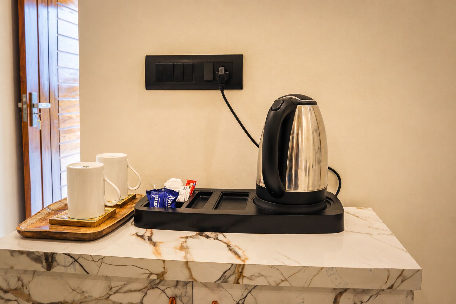 A marble countertop with a coffee maker, two white mugs, and a tray with packets.
