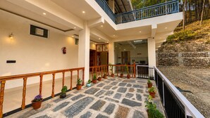 A multi-level building with a stone-tiled floor, wooden railings, and potted plants. - Shikhar Homestay (Lansdowne)